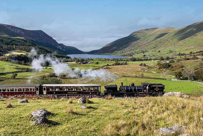 One of the vintage steam trains from Blaenau Ffestiniog Railway going past a lake and mountain in Wales