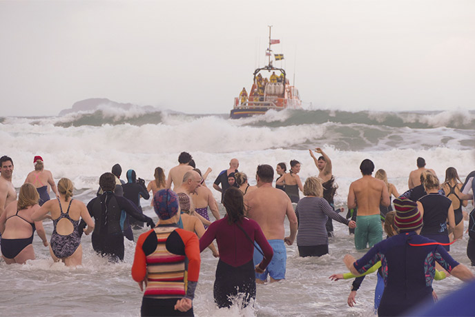 A group of people running into the sea at Whitesands for the New Year's Day Swim with the St Davids Penknife Club