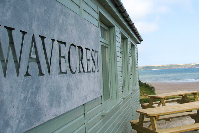 The aqua coloured wooden exterior of Wavecrest Café with the beach in the background