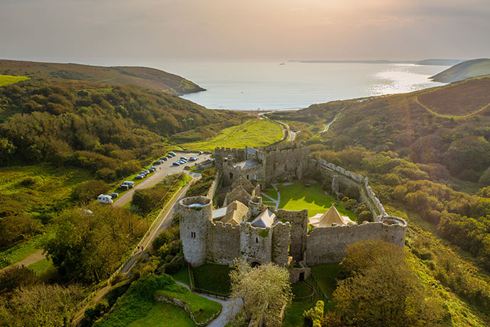 Looking down at Manorbier Castle surrounded by countryside with Manorbier beach and the sea in the distance