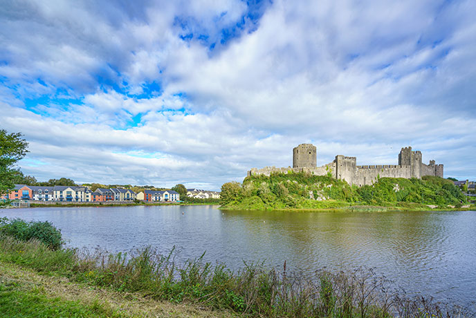 The impressive Pembroke Castle surrounded by water and the colourful houses of Pembroke