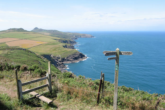 A sty and coast path sign with St David's Head and the ocean in the background