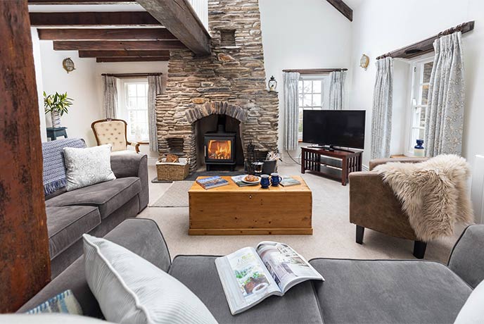 The pretty living room at Towyn Cottage in Pembrokeshire with an expose stone wall and lit wood-burner