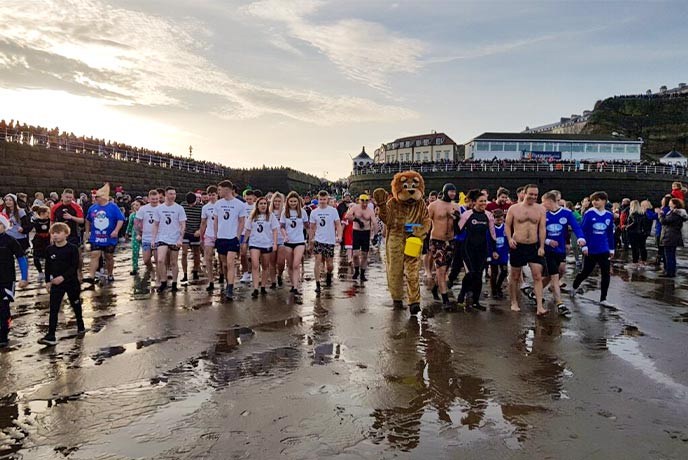 A crowd of people in fancy dress running down the beach during the Boxing Day swim at Whitby in Yorkshire