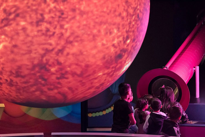 Children gathered around a telescope under a giant planet at the Wanderlab in the National Science and Media Museum in Yorkshire